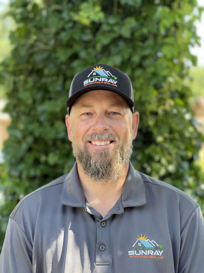 A man with a beard and hat standing in front of a tree.