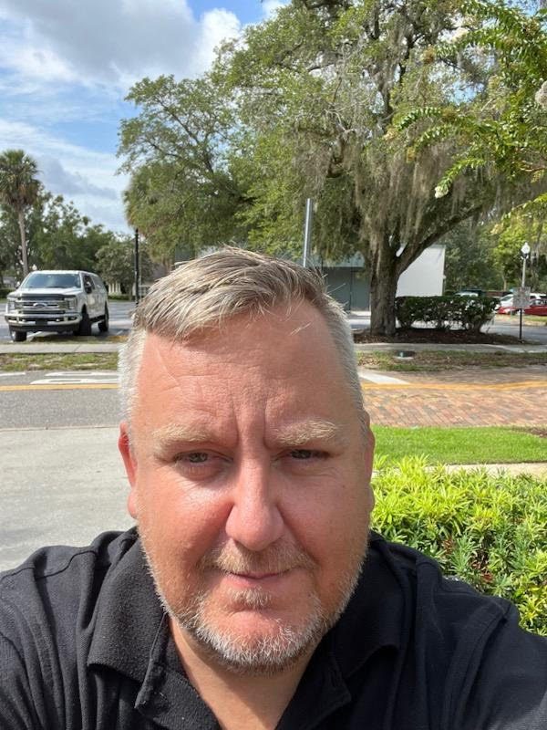 A man with gray hair and glasses is taking a selfie.