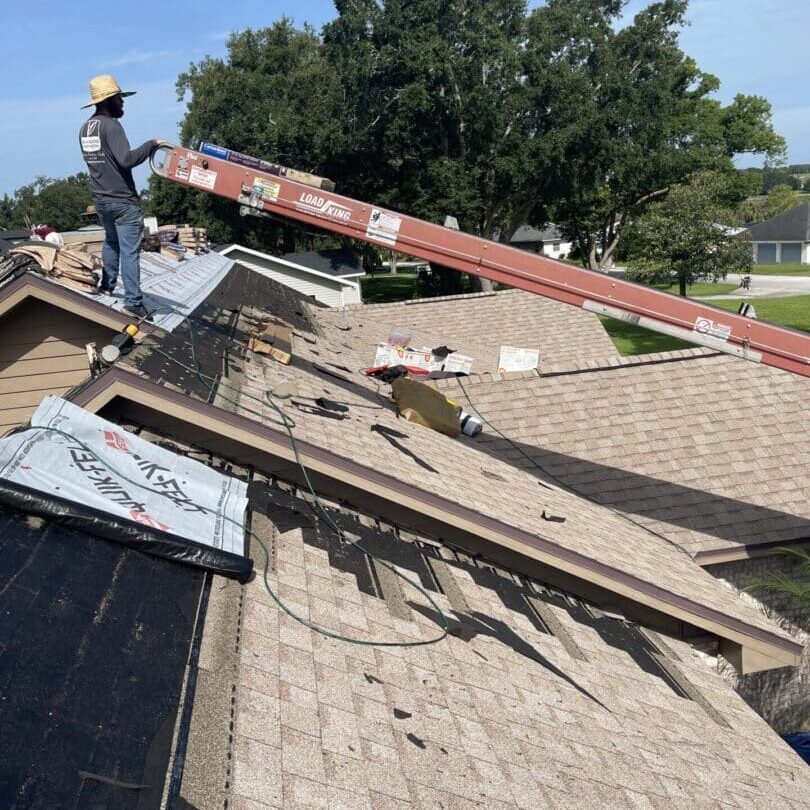 A man standing on top of a roof holding onto the ladder.